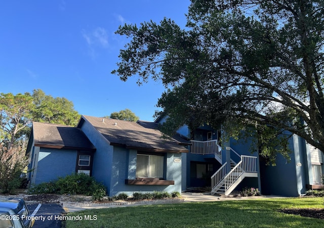 view of front of home featuring roof with shingles, stucco siding, stairway, and a front yard