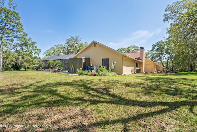 7353 Dogwood, Spring Hill, FL 34607 - rear view of house featuring central AC unit, stucco siding, a chimney, and a lawn