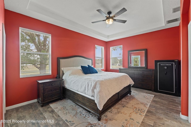 bedroom featuring baseboards, a tray ceiling, wood finished floors, and visible vents