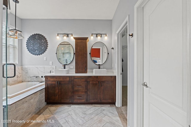 full bath with a sink, a shower with shower door, a garden tub, and double vanity