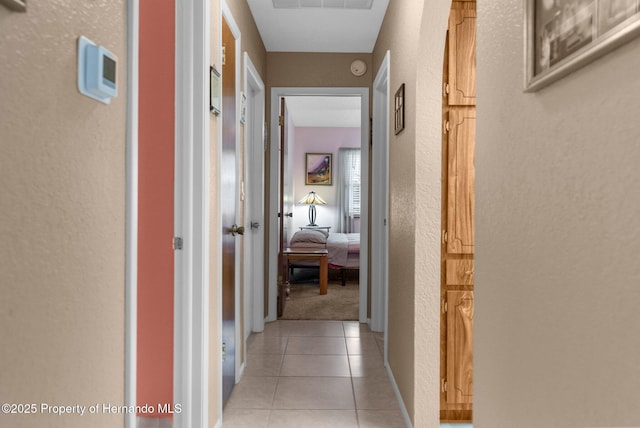 corridor with a textured wall, baseboards, light tile patterned floors, and visible vents