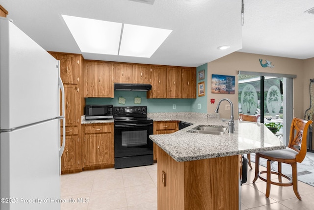 kitchen with a sink, a peninsula, freestanding refrigerator, under cabinet range hood, and black / electric stove