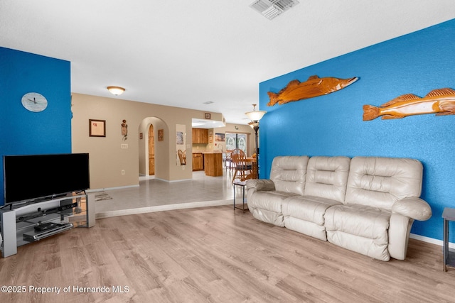 living area with arched walkways, baseboards, visible vents, and wood finished floors