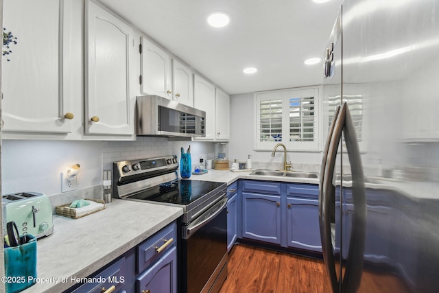 4008 Passport Ln, New Port Richey, FL 34653 - kitchen with stainless steel appliances, a sink, white cabinetry, blue cabinets, and dark wood-type flooring