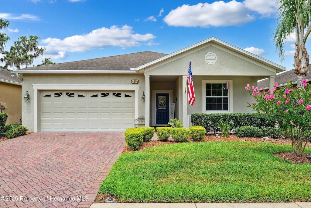 ranch-style home with a garage, decorative driveway, stucco siding, and a front yard