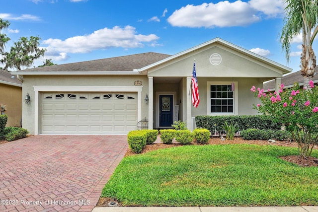 ranch-style home with a garage, decorative driveway, stucco siding, and a front yard