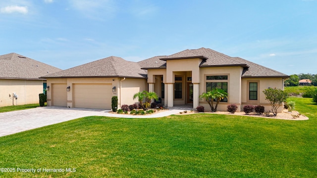 prairie-style home featuring stucco siding, decorative driveway, a garage, a front yard, and roof with shingles