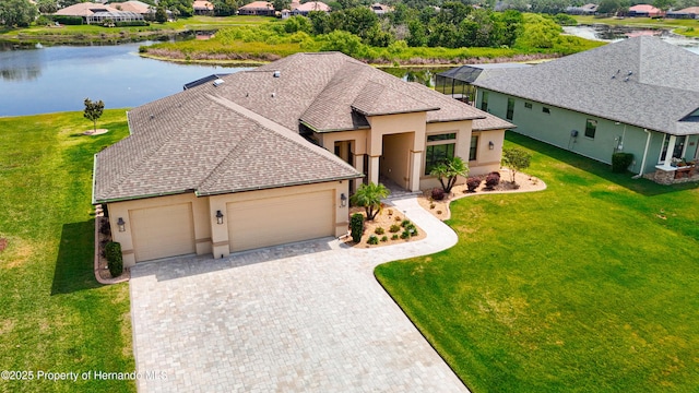 view of front of house with stucco siding, an attached garage, decorative driveway, a water view, and a front yard