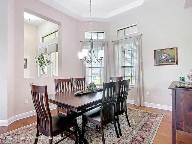 dining space featuring a chandelier, a raised ceiling, wood finished floors, baseboards, and a high ceiling