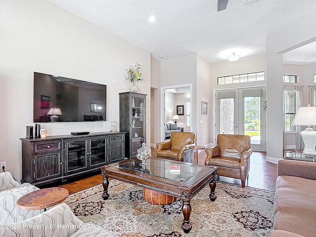 living room featuring ceiling fan, wood finished floors, a high ceiling, baseboards, and french doors