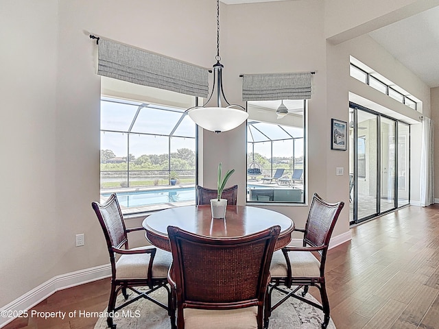 dining room with a sunroom, baseboards, dark wood-style flooring, a high ceiling, and a water view