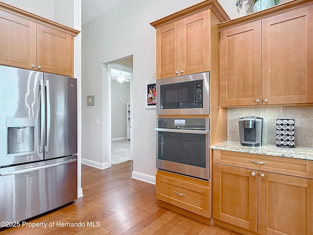 kitchen with stainless steel appliances, baseboards, decorative backsplash, light wood-type flooring, and light stone countertops
