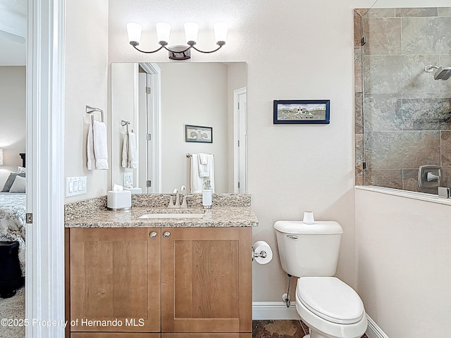 ensuite bathroom featuring tiled shower, toilet, vanity, and baseboards