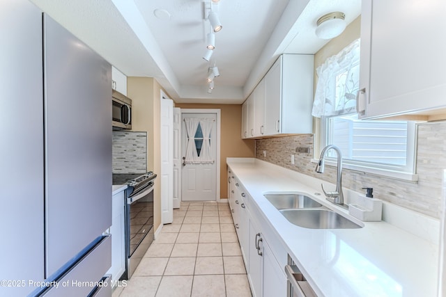 4446 San Juan Dr, Hernando Beach, FL 34607 - kitchen with stainless steel appliances, a sink, light tile patterned floors, track lighting, and white cabinetry