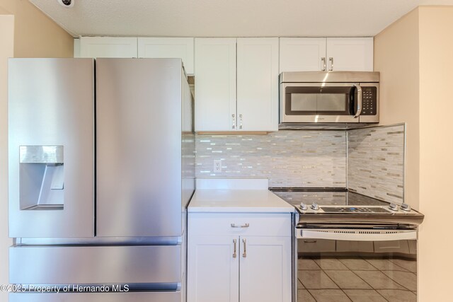 4446 San Juan Dr, Hernando Beach, FL 34607 - kitchen featuring stainless steel appliances, light tile patterned floors, white cabinetry, backsplash, and light countertops
