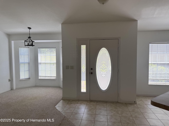 foyer entrance featuring healthy amount of natural light, a chandelier, light tile patterned flooring, and baseboards
