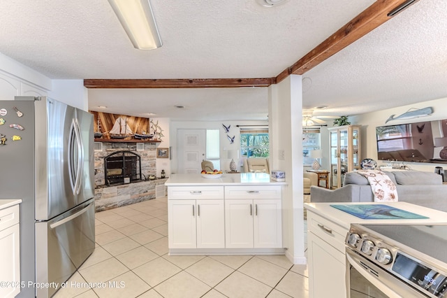kitchen with appliances with stainless steel finishes, open floor plan, a stone fireplace, light tile patterned flooring, and a textured ceiling