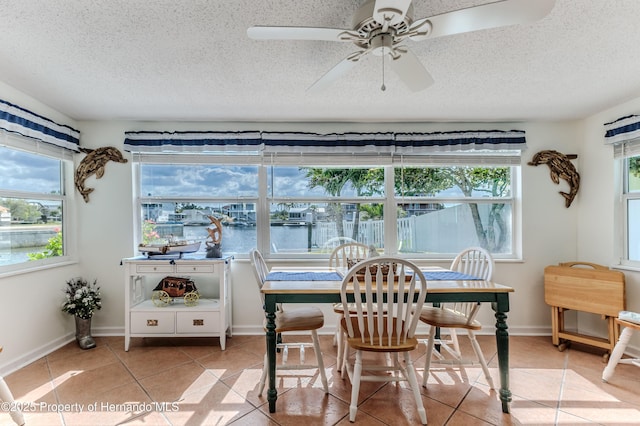 sunroom with tile patterned flooring, a textured ceiling, a water view, and baseboards