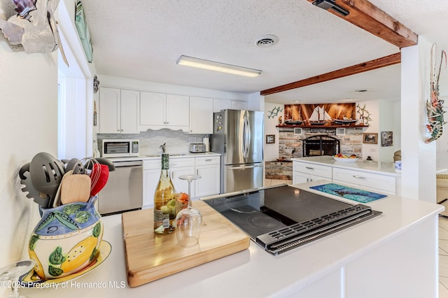 kitchen featuring freestanding refrigerator, white microwave, tasteful backsplash, white cabinetry, and black electric stovetop