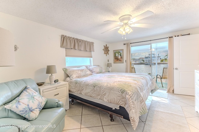 bedroom featuring access to exterior, light tile patterned floors, a water view, a textured ceiling, and a ceiling fan