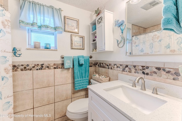 bathroom featuring tile walls, toilet, a textured ceiling, wainscoting, and vanity