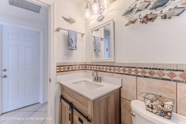 bathroom featuring tile walls, toilet, tile patterned flooring, vanity, and wainscoting