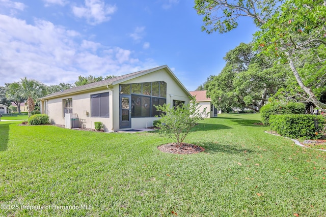 rear view of house featuring stucco siding, a lawn, a sunroom, and central AC unit