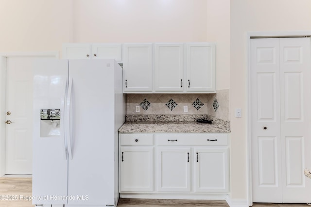 kitchen with white refrigerator with ice dispenser, white cabinets, light stone countertops, decorative backsplash, and light wood-style flooring