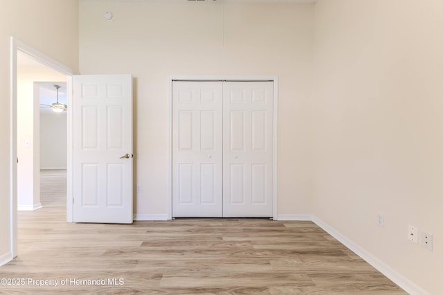 unfurnished bedroom featuring light wood finished floors, baseboards, and a closet