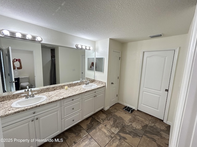 15585 Rene Ct, Brooksville, FL 34604 - bathroom featuring toilet, double vanity, a textured ceiling, stone finish floors, and baseboards
