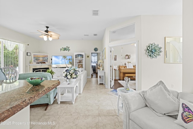 living room featuring a ceiling fan, light tile patterned flooring, and a fireplace
