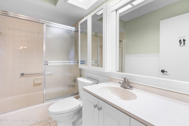 full bathroom featuring toilet, vanity, combined bath / shower with glass door, and a wainscoted wall
