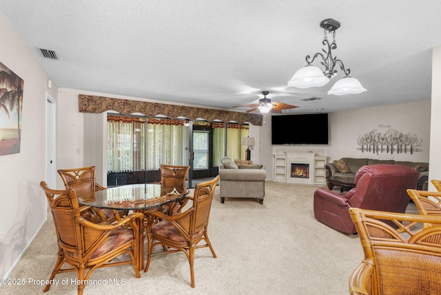 dining room with light colored carpet, a warm lit fireplace, a textured ceiling, and ceiling fan