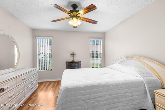 bedroom featuring light wood finished floors, multiple windows, baseboards, a textured ceiling, and a ceiling fan