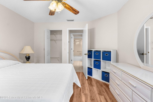 bedroom featuring light wood-type flooring, a ceiling fan, and a walk in closet