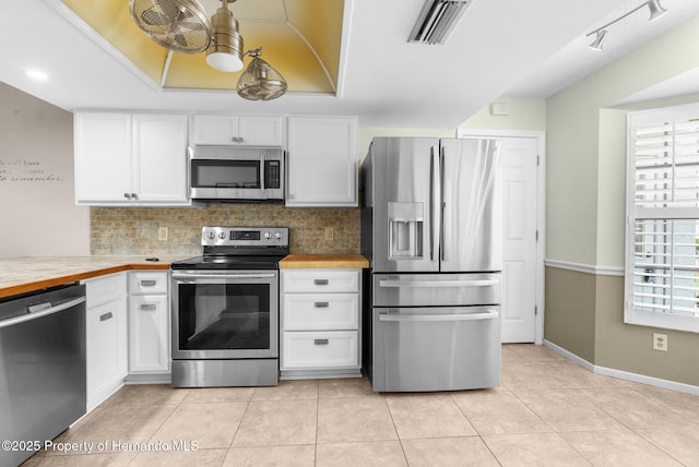 kitchen with appliances with stainless steel finishes, white cabinetry, tasteful backsplash, light tile patterned floors, and baseboards