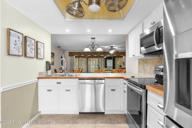 kitchen featuring appliances with stainless steel finishes, a peninsula, a chandelier, a sink, and recessed lighting
