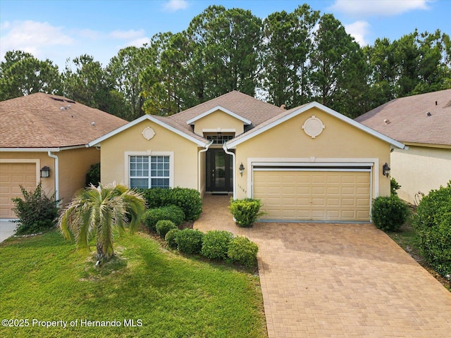ranch-style home with a garage, stucco siding, decorative driveway, and a front lawn