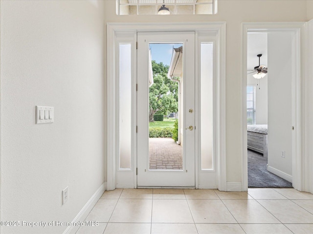 doorway featuring healthy amount of natural light, baseboards, light tile patterned floors, and a ceiling fan