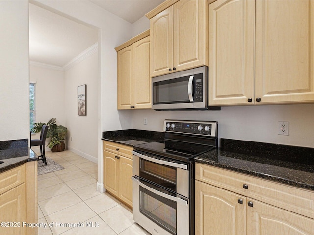 kitchen with appliances with stainless steel finishes, light brown cabinetry, crown molding, dark stone counters, and light tile patterned flooring