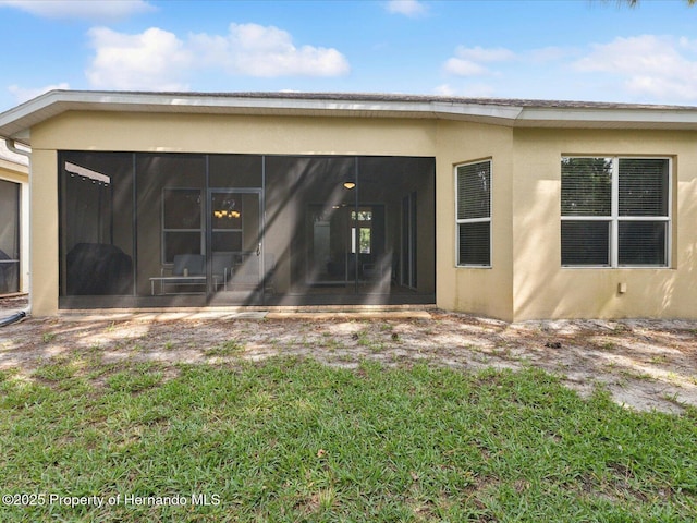 back of property with a sunroom, stucco siding, and a yard