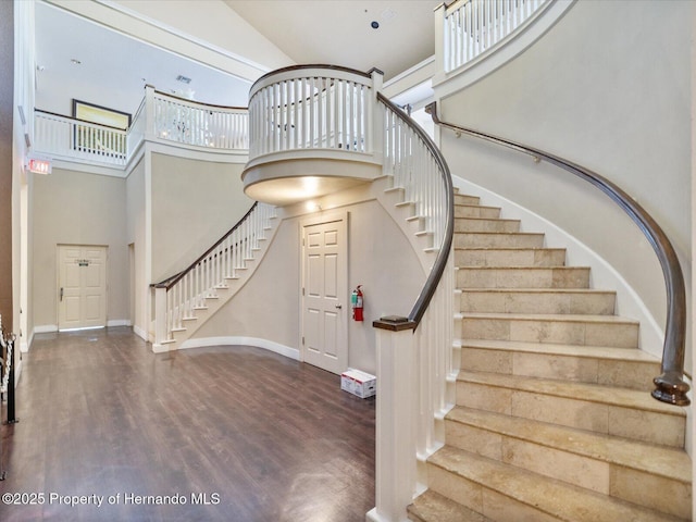 stairs featuring a towering ceiling, wood finished floors, and baseboards