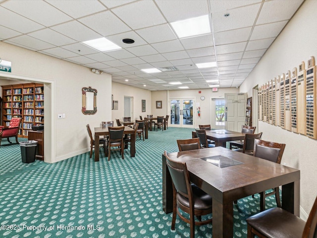 carpeted dining area with a paneled ceiling and baseboards