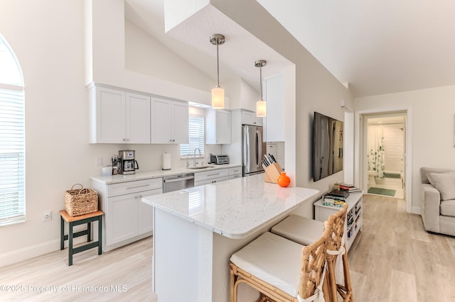 kitchen with stainless steel appliances, vaulted ceiling, a sink, light wood finished floors, and a kitchen breakfast bar