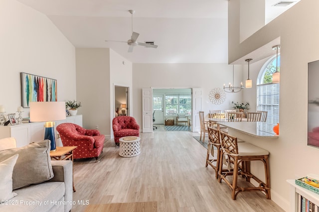 living room featuring high vaulted ceiling, light wood-type flooring, ceiling fan, baseboards, and a chandelier