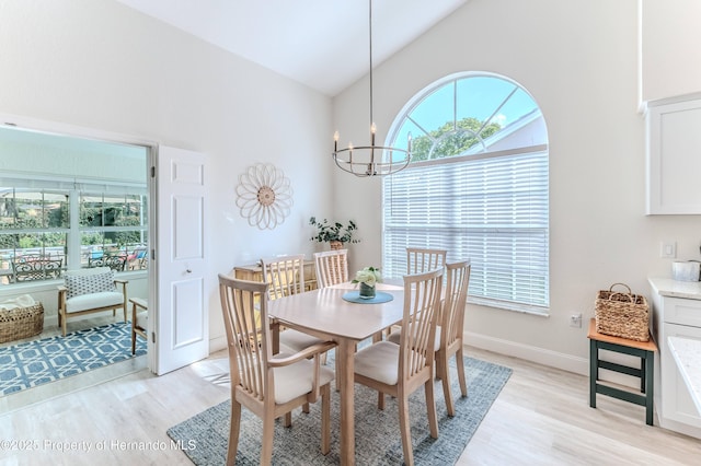 dining space featuring light wood finished floors, high vaulted ceiling, healthy amount of natural light, and a chandelier