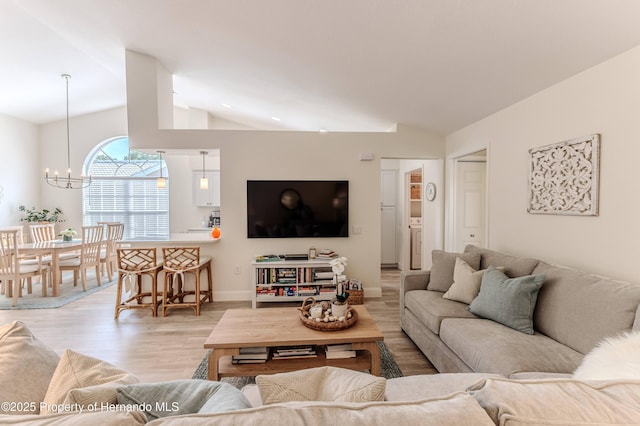 living room with lofted ceiling, a chandelier, light wood-style floors, washer / dryer, and baseboards