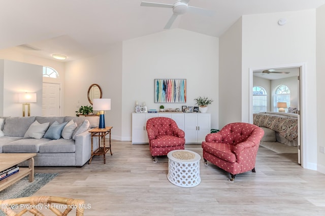 living room with ceiling fan, light wood-style floors, baseboards, and vaulted ceiling