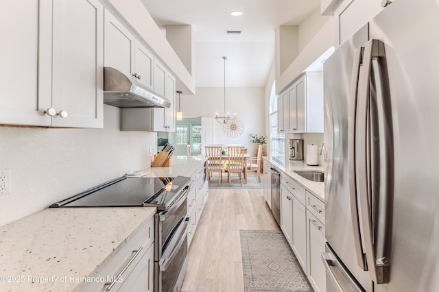 kitchen featuring appliances with stainless steel finishes, under cabinet range hood, a chandelier, light wood-style floors, and light stone countertops