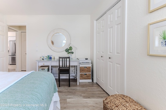 bedroom with stainless steel fridge, wood finished floors, and a closet